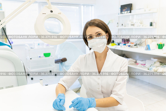 A cute doctor in a white coat. the cosmetologist is sitting in the office and smiling. A magnifying glass for examining the skin. Anti-aging procedures. A dermatologist at his desk. Стоковое фото, фотограф Ирина Ткачук / Фотобанк Лори