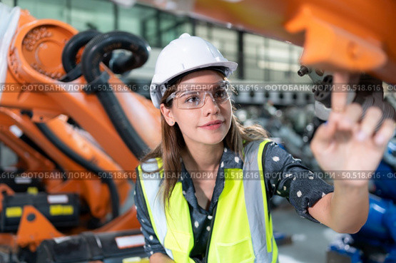 A female engineer installs a program on a robotics arm in a robot warehouse. And test the operation before sending the machine to the customer. Стоковое фото, агентство Ingram Publishing / Фотобанк Лори