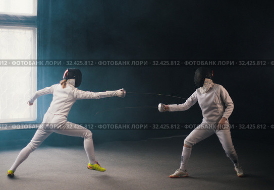 A fencing training in the studio - two women in protective costumes having a duel - pointing swords at each other. Стоковое фото, фотограф Константин Шишкин / Фотобанк Лори