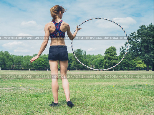 A fit and athletic young woman is twirling a hula hoop in the park on a sunny summer day. Стоковое фото, агентство Ingram Publishing / Фотобанк Лори