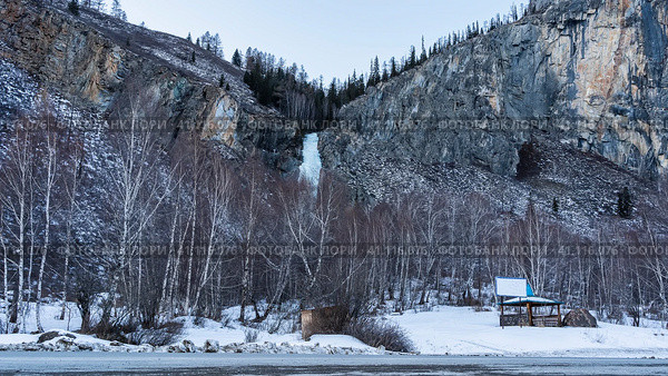 A frozen waterfall is visible in the gorge between the mountain slopes. On the side of the road, in the snowdrifts there is a gazebo, bare trees. Altai. Стоковое фото, фотограф Вера Ивановна Кубарева / Фотобанк Лори