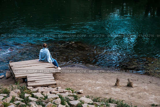 A girl is sitting on the shore of a blue lake. Beautiful natural background. Blue Lake in Kazan. Russia, Republic of Tatarstan, Kazan, September 2023. Стоковое фото, фотограф Photojuli / Фотобанк Лори