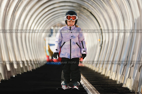 A girl on skis stands on a carpet ski lift in a glass tunnel. Стоковое фото, фотограф Irina Kuchugurina/Gaudy / Фотобанк Лори