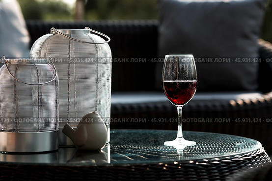 A glass of red alcoholic drink or wine on a glass table on the veranda. The concept of alcoholism, a party, or a holiday. Стоковое фото, фотограф Photojuli / Фотобанк Лори