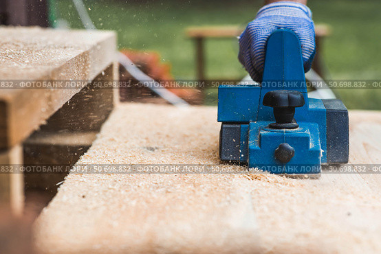 A hand-held electric planer in the hands of a craftsman. A man planing boards with an electric tool. Production of wooden products. Construction, wood processing. Стоковое фото, фотограф Photojuli / Фотобанк Лори