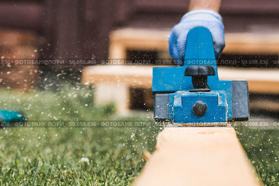A hand-held electric planer in the hands of a craftsman. A man planing boards with an electric tool. Production of wooden products. Construction, wood processing. Стоковое фото, фотограф Photojuli / Фотобанк Лори