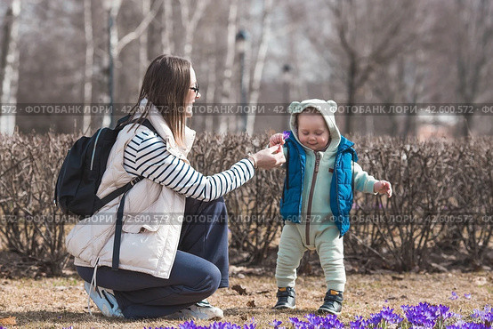 A handsome, cheerful little boy of two years old walks with his mother on the street in the spring. The kid plays and collects flowers for his mother in the park. The concept of parenthood, childhood and family. Стоковое фото, фотограф Photojuli / Фотобанк Лори