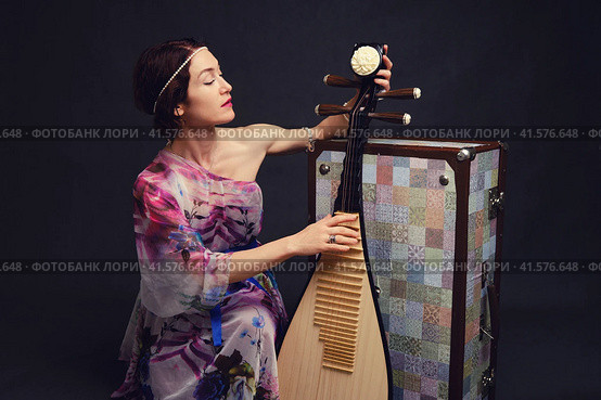 A happy female musician in Asian clothes on a studio black background. A smiling woman with a stringed musical instrument from Asia on a dark background. Стоковое фото, фотограф Андрей Журавлев / Фотобанк Лори