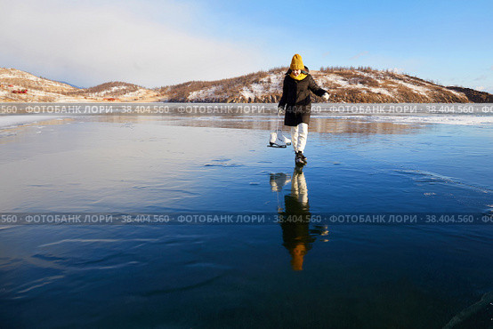 A happy girl looks at her reflection on the ice of the frozen Lake Baikal. He holds skates in his hands. Стоковое фото, фотограф Виктория Тельминова / Фотобанк Лори