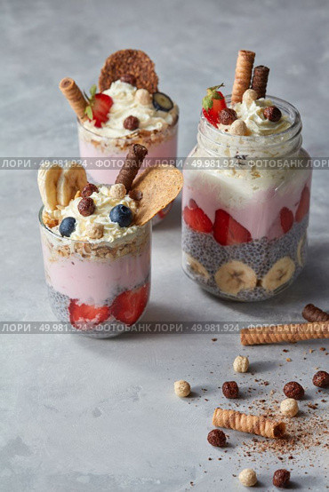 A healthy dessert made of chia seeds with yoghurt, strawberries, biscuits and bananas in glasses on a concrete background. Free space for text.. Chia pudding with yoghurt, honey, strawberry and banana on pastel concrete background. Стоковое фото, агентство Ingram Publishing / Фотобанк Лори