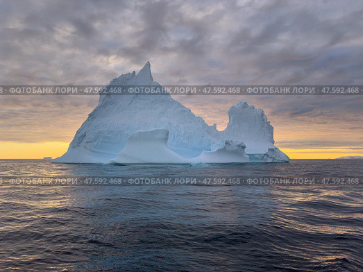 A huge high breakaway glacier drifts in the southern ocean off the coast of Antarctica at sunset, the Antarctic Peninsula, the Southern Arctic Circle, azure water, cloudy weather. Стоковое фото, фотограф Vladimir Drozdin / Фотобанк Лори
