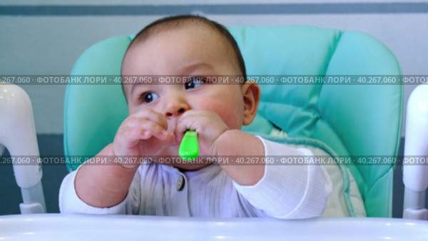 A hungry baby is gnawing on a plastic spoon at the table on a high chair. Teething, whims, itchy gums, introduction of complementary foods. Стоковое видео, видеограф Ольга Симонова / Фотобанк Лори