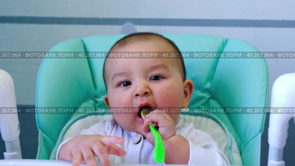 A hungry baby is gnawing on a plastic spoon at the table on a high chair. Teething, whims, itchy gums, introduction of complementary foods. Стоковое видео, видеограф Ольга Симонова / Фотобанк Лори