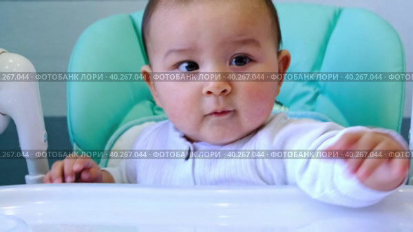 A hungry baby taps his hand on the table on a high chair, asks to eat, nibbles on a spoon. Teething, whims, itchy gums, introduction of complementary foods. Стоковое видео, видеограф Ольга Симонова / Фотобанк Лори