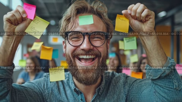A joyful man holds up sticky notes while celebrating ideas in a vibrant workspace filled with colleagues working together creatively. Стоковое AI-видео, аниматор Данила Большаков / Фотобанк Лори