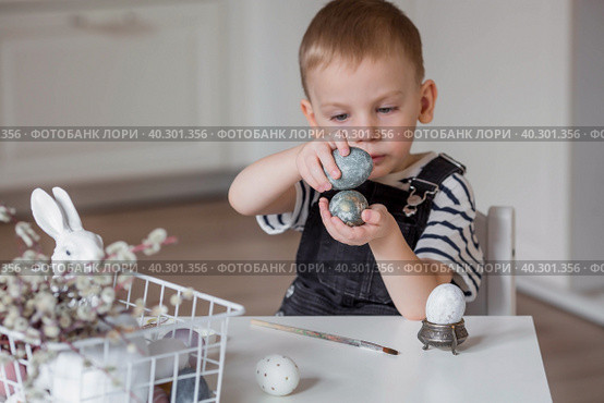 A little boy holds Easter eggs in his hands and hits them against each other. Easter is a bright holiday. A child is playing with eggs. Стоковое фото, фотограф Photojuli / Фотобанк Лори