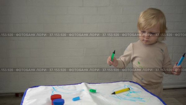 A little girl in pajamas is walking near a table with water markers for children. There is a reusable tablecloth on the table for drawing. Стоковое видео, видеограф Наталья Гармашева / Фотобанк Лори