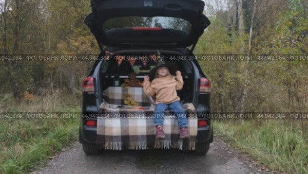 A little girl is sitting in the trunk of a car and wearing a witch hat for the Halloween holiday. The concept of children's Halloween. Стоковое видео, видеограф Терехова Марина / Фотобанк Лори