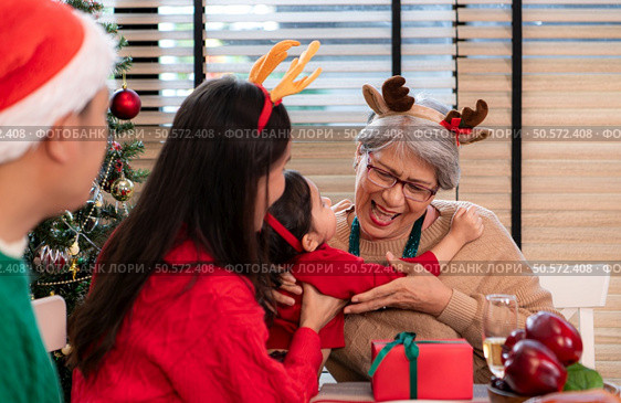 A little granddaughter lovingly hugs her grandmother, while they eating a meal together during the Christmas celebration at home. Стоковое фото, агентство Ingram Publishing / Фотобанк Лори