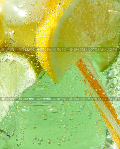 A macro shot of a glass with a cold refreshing lemonade with ice, pieces of lime, lemon and mint leaves, plastic straws on a green background. Bubbles of air in a glass jar.. Close-up of sparkling fresh lemonade with ice, slices of lime and lemon, leaf of mint with plastic straws. Large bubbles of air on a green background. Стоковое фото, агентство Ingram Publishing / Фотобанк Лори