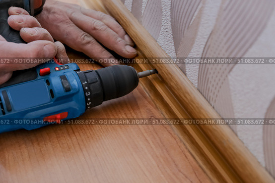 A male repairman installs baseboards at home. Room renovation... Стоковое фото, фотограф lyudmila Soloveva / Фотобанк Лори