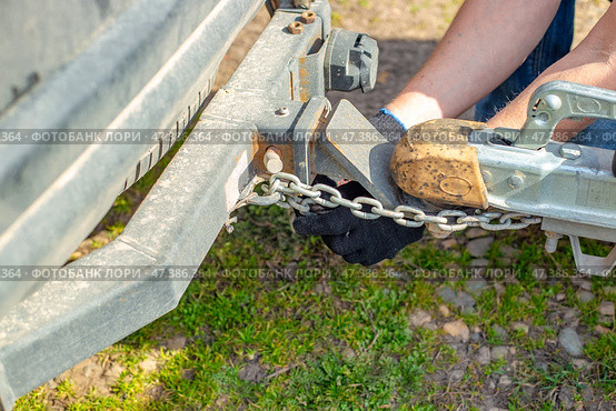 A man attaches a trailer to a car, securing safety chains to the trailer's hitch and drawbar. Стоковое фото, фотограф Коханова Наталья / Фотобанк Лори