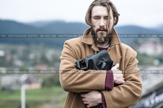 a man in a brown coat stands clutching a black briefcase on a background of mountains. Стоковое фото, агентство Ingram Publishing / Фотобанк Лори