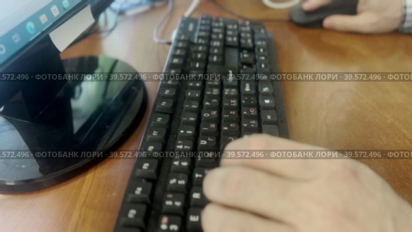 A man in a plaid shirt sits down at his desk in the office and starts typing on a computer keyboard. A sketch from the office. Стоковое видео, видеограф Ярославский Максим / Фотобанк Лори