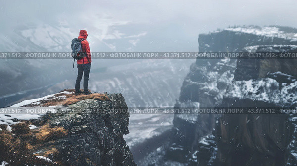 A man in a red jacket with a hood and a backpack stands on the edge of a cliff. There is snow all around, snow-capped mountains and gorges are visible, creating an atmosphere of solitude and severity. The sky is overcast and snowing. The landscape conveys a feeling of coldness and the power of nature, and the person looks determined and ready for new challenges. Стоковое AI-изображение, AI-художник Анна Кривицкая / Фотобанк Лори
