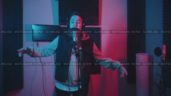 A man in hoodie rapping in the studio gesticulates while recording his track. Стоковое видео, видеограф Константин Шишкин / Фотобанк Лори