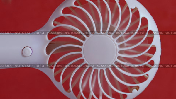 A man presses the power button on a portable portable fan. Demonstrates operating modes, then turns off. The propeller gradually stops. On a coral background. Close-up. Стоковое видео, видеограф Vadzim Yakubovich / Фотобанк Лори