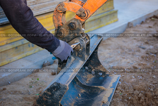 A man repairs a tractor bucket, changes the mounting sleeve. Replacing the nozzle on the tractor boom. Close-up. Стоковое фото, фотограф Юрий Поздников / Фотобанк Лори