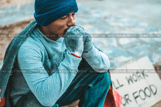 a man sitting beggars with homeless please help message. Selective focus. Стоковое фото, агентство Ingram Publishing / Фотобанк Лори