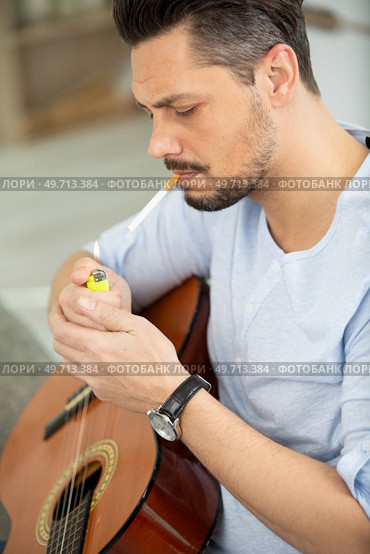 a man smokes while playing guitar. Стоковое фото, агентство Ingram Publishing / Фотобанк Лори