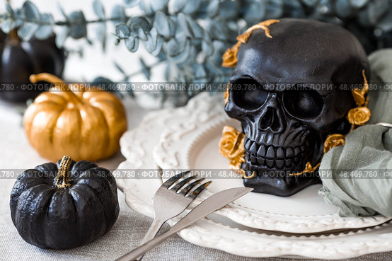 A mysterious black skull with golden roses and pumpkins on serving plates for a Halloween or Day of the Dead party. Стоковое фото, фотограф Photojuli / Фотобанк Лори