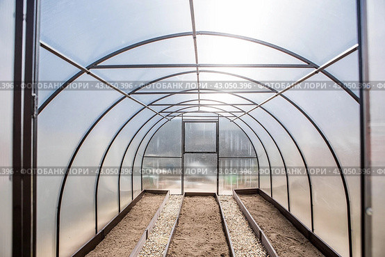 A new greenhouse made of polyethylene and polycarbonate with new beds made of Wood-polymer composite. Preparing for the spring garden season. Installation of a greenhouse in a suburban area. Стоковое фото, фотограф Photojuli / Фотобанк Лори