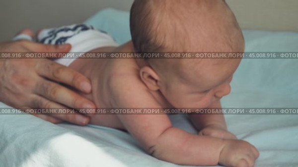 A newborn baby lying on its stomach and trying to hold its head. Close-up. A parent's hand is supporting the baby from the side so that he does not turn over. Стоковое видео, видеограф Воловодов Владимир / Фотобанк Лори