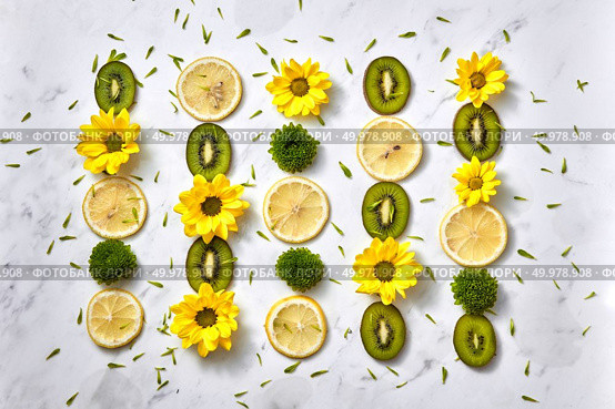 A pattern of even rows from yellow, green flowers, fruits kiwi, lemon slices and green petals. Floral composition, flowers background. Top view. Floral background. Flowers pattern from yellow, green flowers, slices of kiwi and lemon. Flat lay. Стоковое фото, агентство Ingram Publishing / Фотобанк Лори