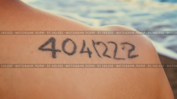 A person shows their tattoo of the number 404222 on their shoulder as waves crash in the background. Стоковое AI-видео, аниматор Данила Большаков / Фотобанк Лори