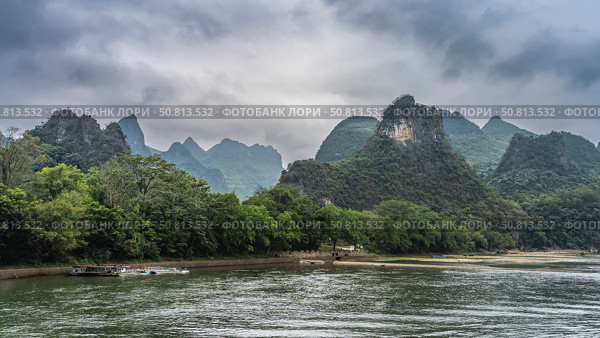 A picturesque river. Tourist ships are moored at the marina. Green vegetation on the shore. Mountains against the sky and clouds. China. Li River. Li Jiang. Guilin. Стоковое фото, фотограф Вера Ивановна Кубарева / Фотобанк Лори