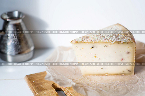 A piece of fresh, aged, natural farm cheese on parchment on a wooden board. Quality of farm-fresh agricultural products. Стоковое фото, фотограф Photojuli / Фотобанк Лори