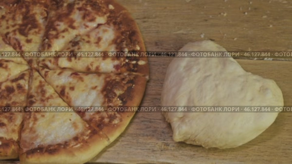 A piece of heart-shaped rye dough next to a finished pizza made from baked cheese and tomato dough. Close up. Стоковое видео, видеограф Strunov David / Фотобанк Лори