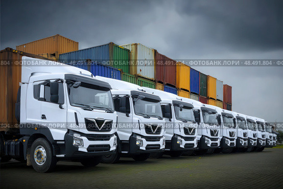 A row of white trucks are parked in front of a row of green containers. Стоковое AI-изображение, AI-художник Ярославский Максим / Фотобанк Лори
