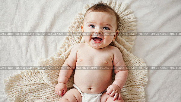 A small child is lying on a bed wrapped in an intricately tied blanket, top view. A child in the first moments of his life looks at the world and smiles. Стоковое AI-изображение, AI-художник Антон Слабоспицкий / Фотобанк Лори