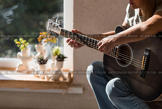 A talented young female musician sits alone and composes songs on the guitar. She plays a calm melody on a musical instrument.Music and hobbies. Стоковое фото, фотограф Photojuli / Фотобанк Лори