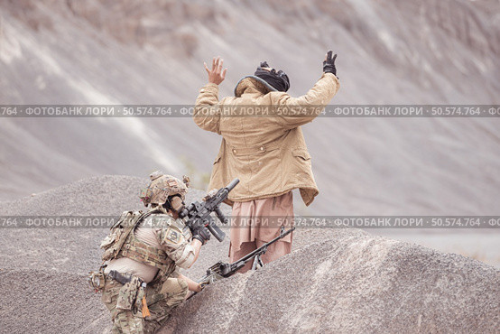 A Taliban soldier stands with a machine gun, Raise hands in surrender to the allied soldiers, In the desert mountain terrain battlefield. Стоковое фото, агентство Ingram Publishing / Фотобанк Лори