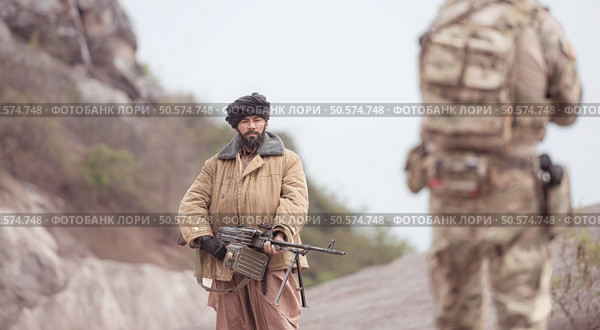A Taliban soldier stands with a machine gun, Surrender to the allied soldiers, In the desert mountain terrain battlefield. Стоковое фото, агентство Ingram Publishing / Фотобанк Лори