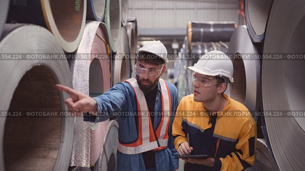 A team of young men working in a warehouse storing rolls of metal sheets. Inspecting the metal sheet rolls stored in the warehouse to be imported onto the metal sheet production line. Стоковое фото, агентство Ingram Publishing / Фотобанк Лори