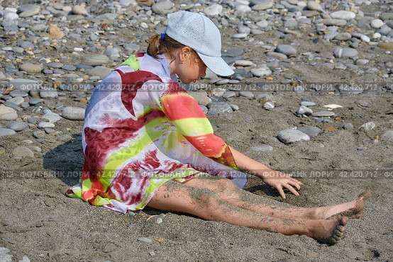 A teenage girl in a cap and a pareo is sitting on a pebble beach. Стоковое фото, фотограф Светлана Семёновская / Фотобанк Лори