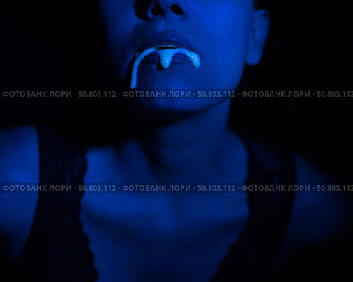 A thick white liquid flows down the lips of a young European girl. Dripping down. Ultraviolet, blue light. Close-up portrait. Spit out. Стоковое фото, фотограф Михаил Решетников / Фотобанк Лори